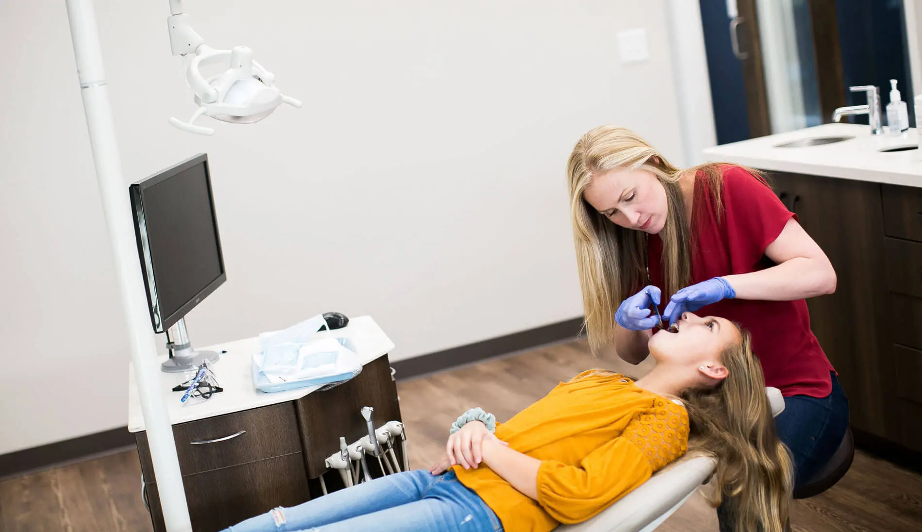 A child sits in a dental chair while a children’s orthodontist, wearing gloves, cleans her teeth with a dental tool in Charlotte, Indian Trail and Monroe, NC.