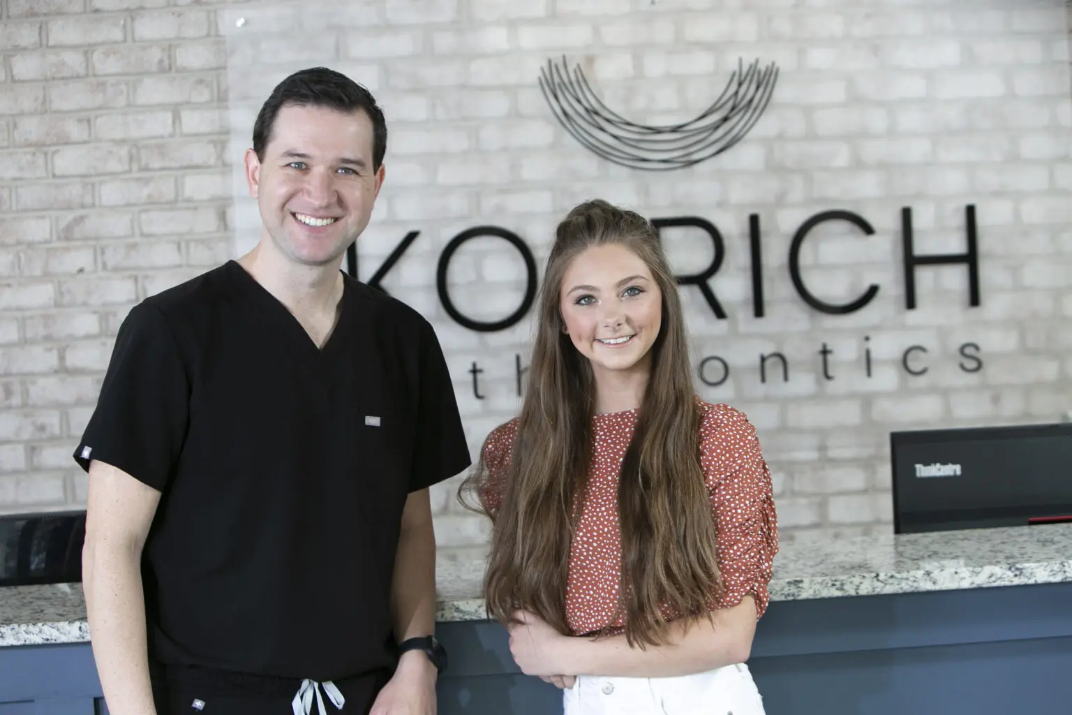 Dr. Leo and a patient smile in front of the reception desk at Koerich Orthodontics, serving patients invisalign in Charlotte, Indian Trail, or Monroe, NC.