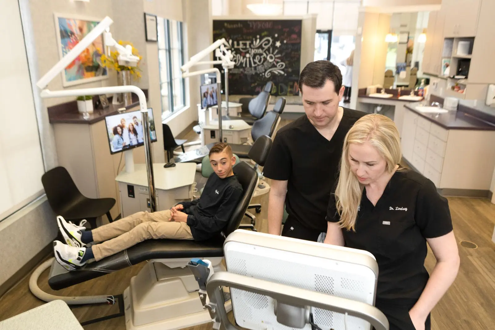At Koerich Orthodontics in Charlotte, Indian Trail or Monroe, NC, two dental professionals review a monitor to track a young patient's progress with clear aligners in a modern clinic setting.