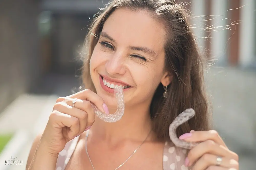 a woman smiling while holding two invisalign clear aligners as one of the alternatives to braces in charlotte and indian trails, nc