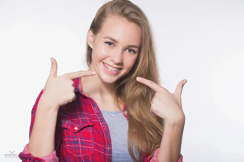 a woman with metal braces pointing at her teeth after considering between aligners vs braces in Charlotte, NC