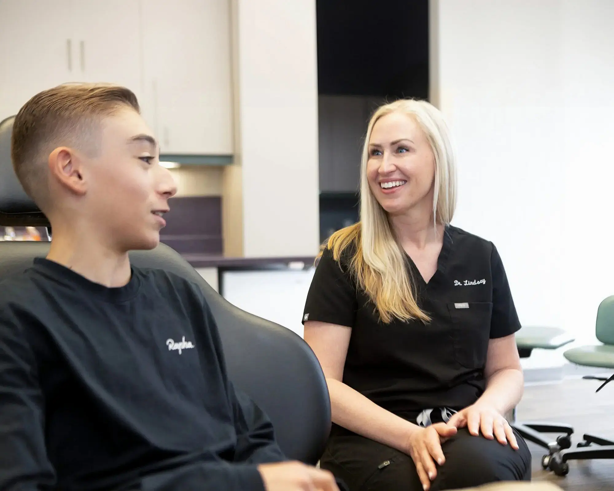 A dentist in black scrubs smiles warmly as they discuss the young patient's braces in the dental office in Charlotte, NC