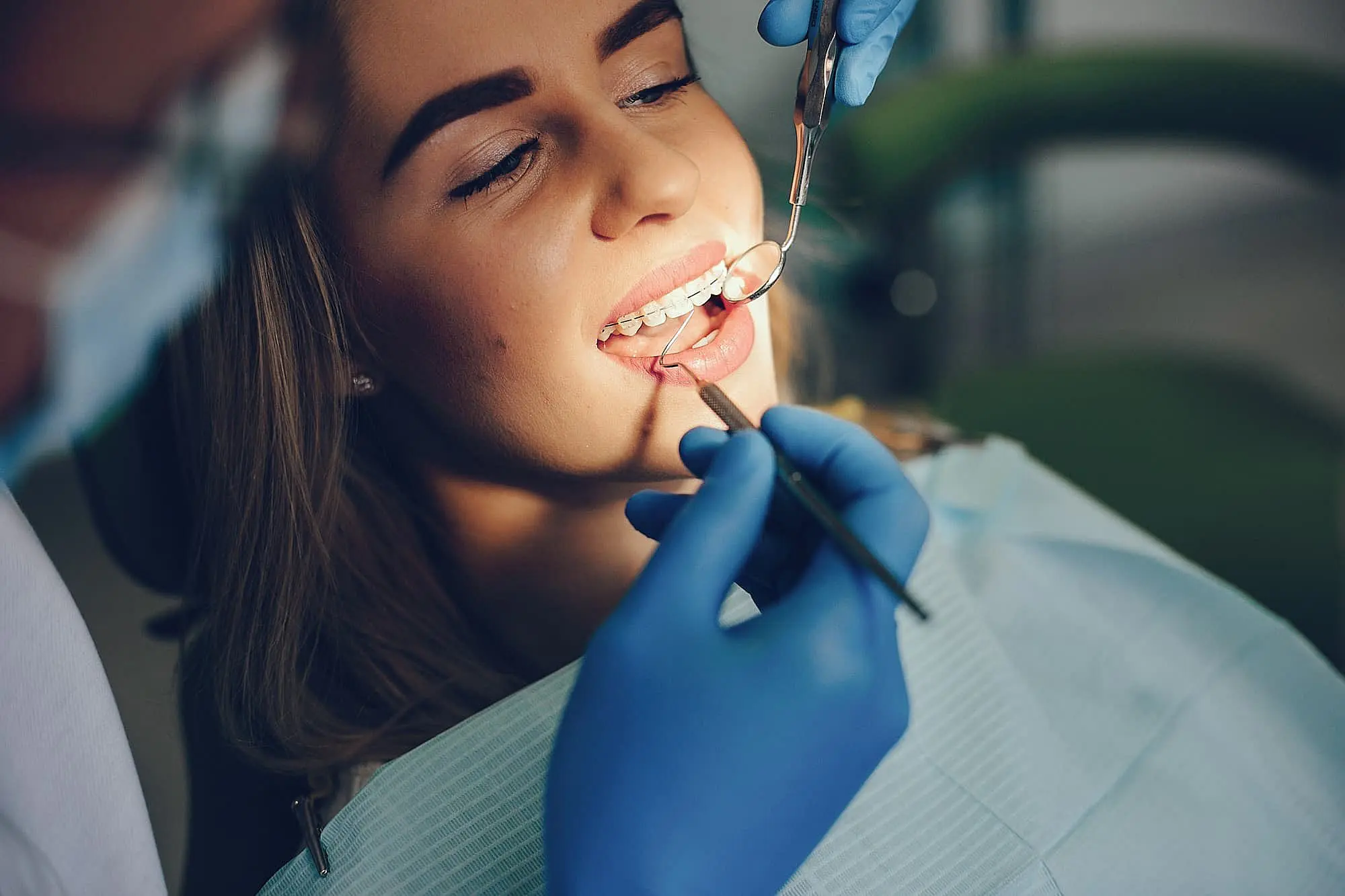 A person receives a dental checkup; a dentist in gloves holds a dental mirror and tool near the person's teeth, discussing the benefits of clear braces for enhancing that perfect smile in Charlotte, NC