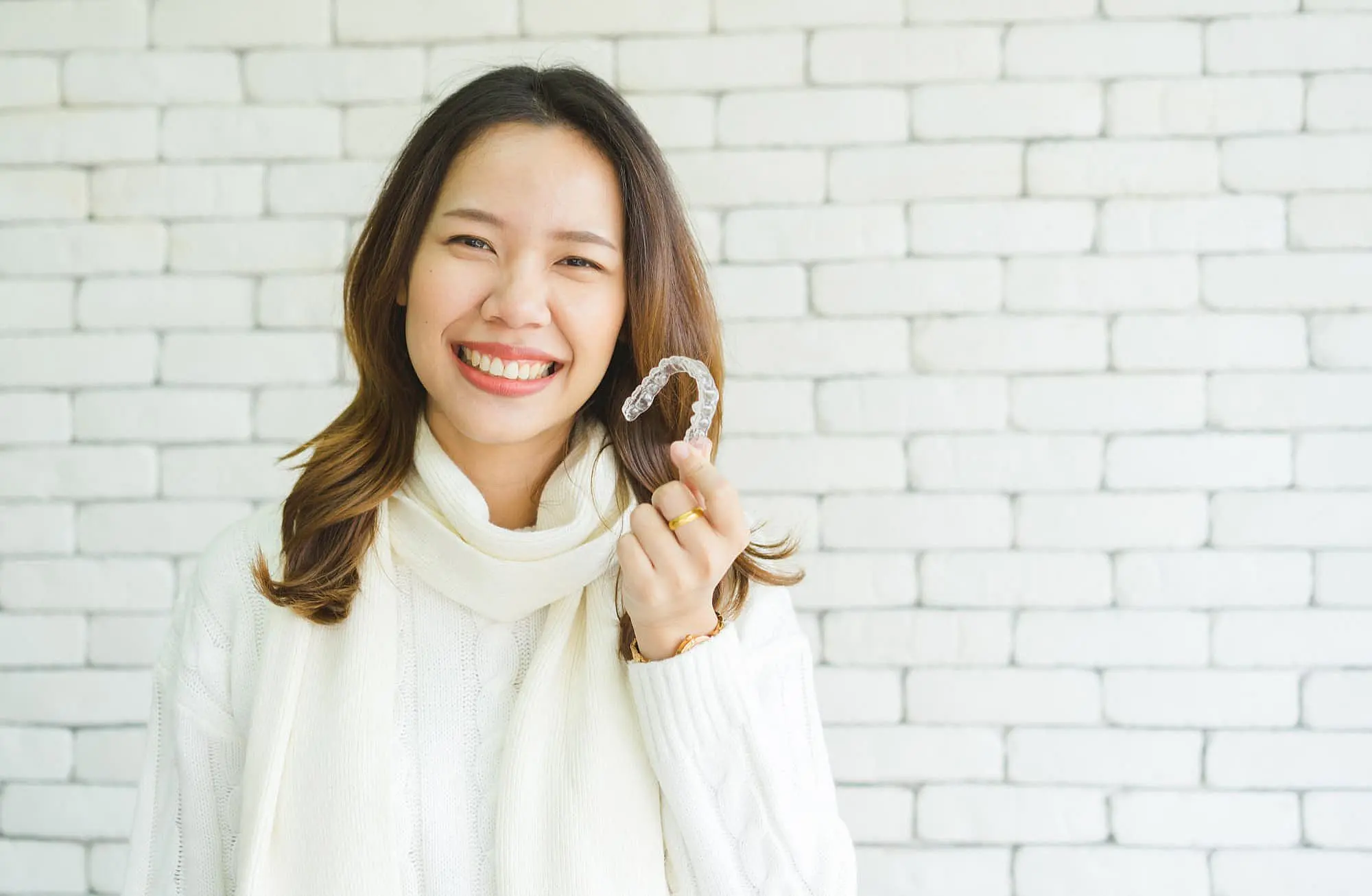 A woman smiles warmly as she holds invisalign, showcasing the best service orthodontics at Koerich Orthodontics in Charlotte, NC