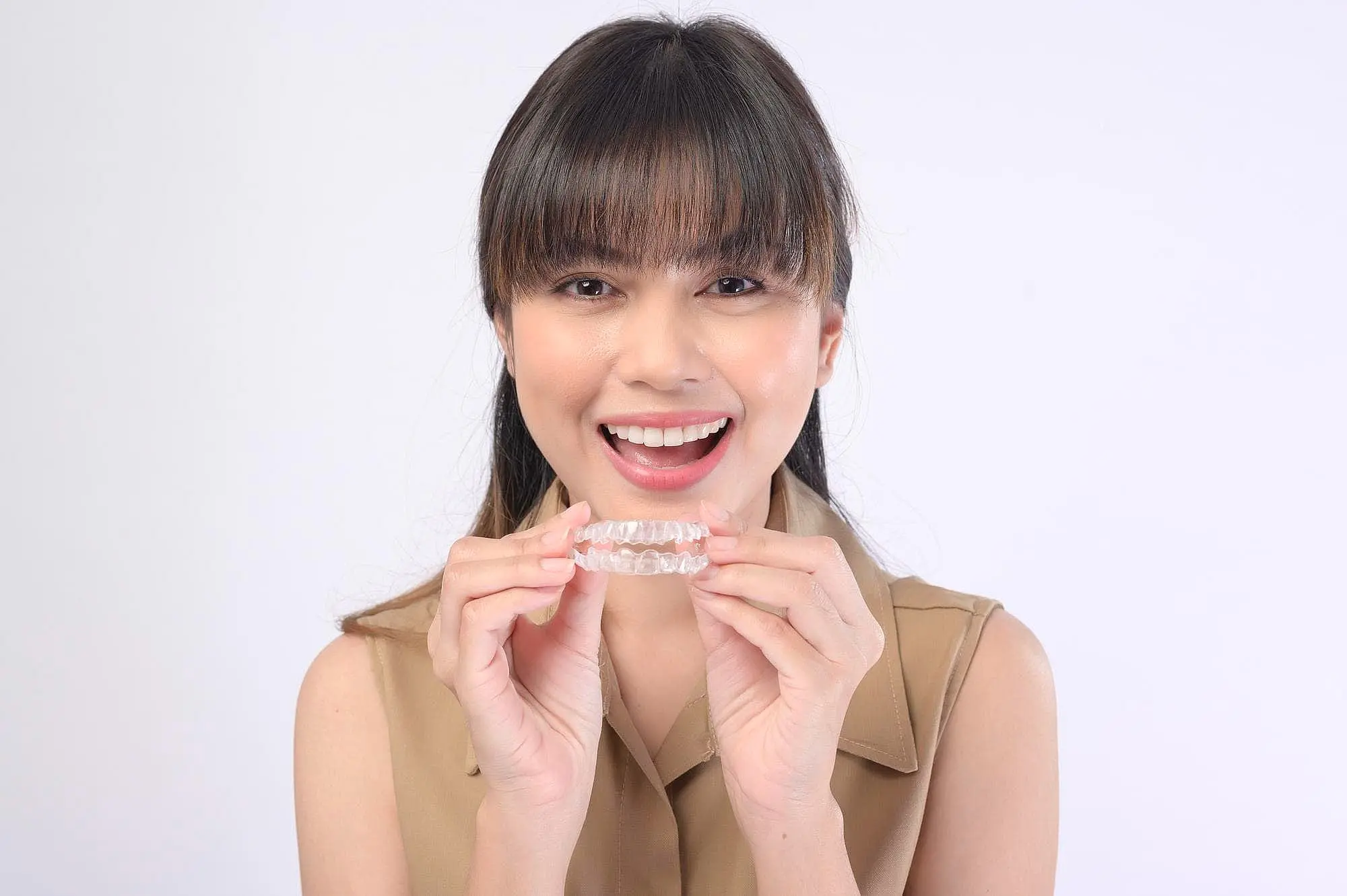 A woman smiling and holding invisalign, a testament to the best orthodontics innovation at Koerich Orthodontics in Charlotte, NC