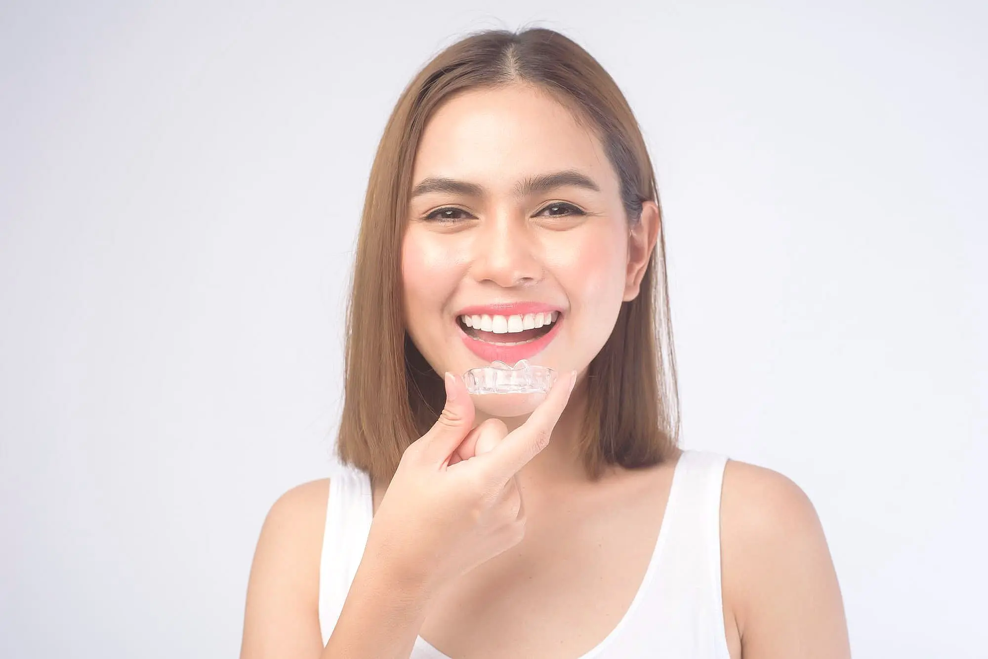 A woman smiles as she holds invisalign, showcasing the best service orthodontics from Koerich Orthodontics in Indian Trail, NC.