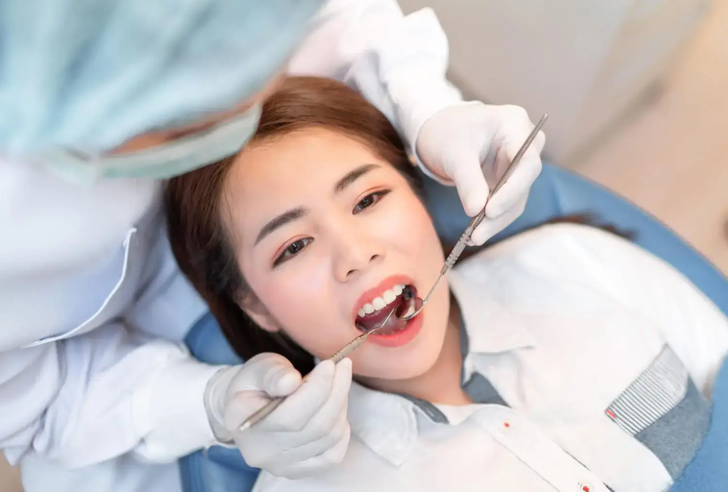 A dentist uses a dental mirror and probe to examine a young woman's teeth while she sits in the dental chair for begin use palatal expander in Charlotte, Indian Trail or Monroe, NC.