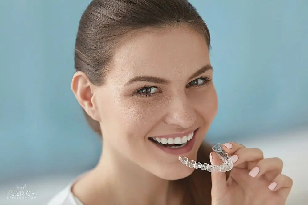 A woman smiles as she prepares to insert a clear dental aligner, showcasing the effective treatment available at Koerich Orthodontics in Charlotte, Indian Trail, or Monroe, NC.