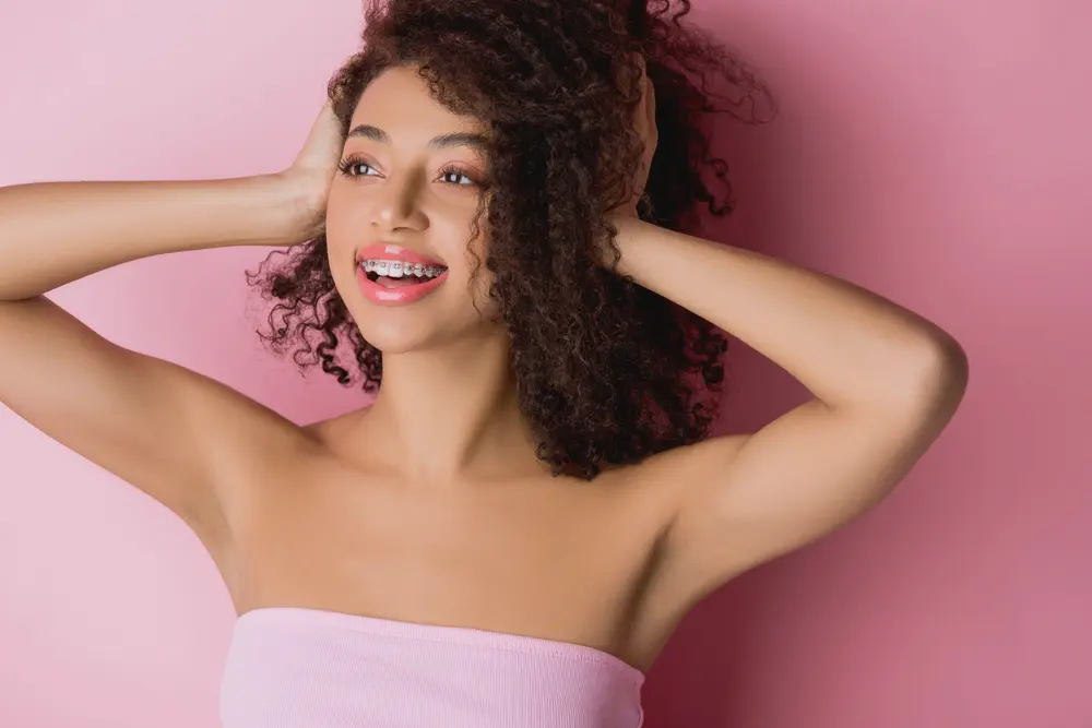 A young woman in a pink tube top with braces smiles confidently, highlighting Koerich Orthodontics in Charlotte, Indian Trail or Monroe, NC - How to Clean Braces in Charlotte, NC