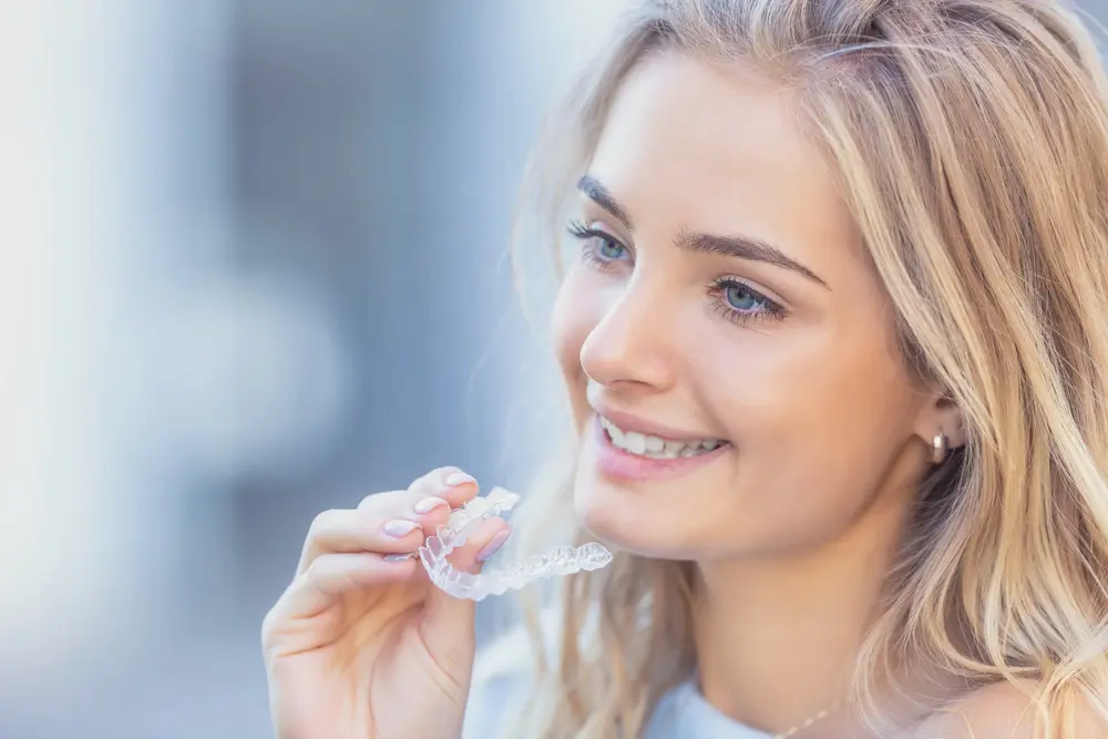A woman prepares to place a clear dental aligner over her teeth at Koerich Orthodontics in Charlotte, Indian Trail or Monroe, NC - How Long Does Invisalign Take in Charlotte, NC