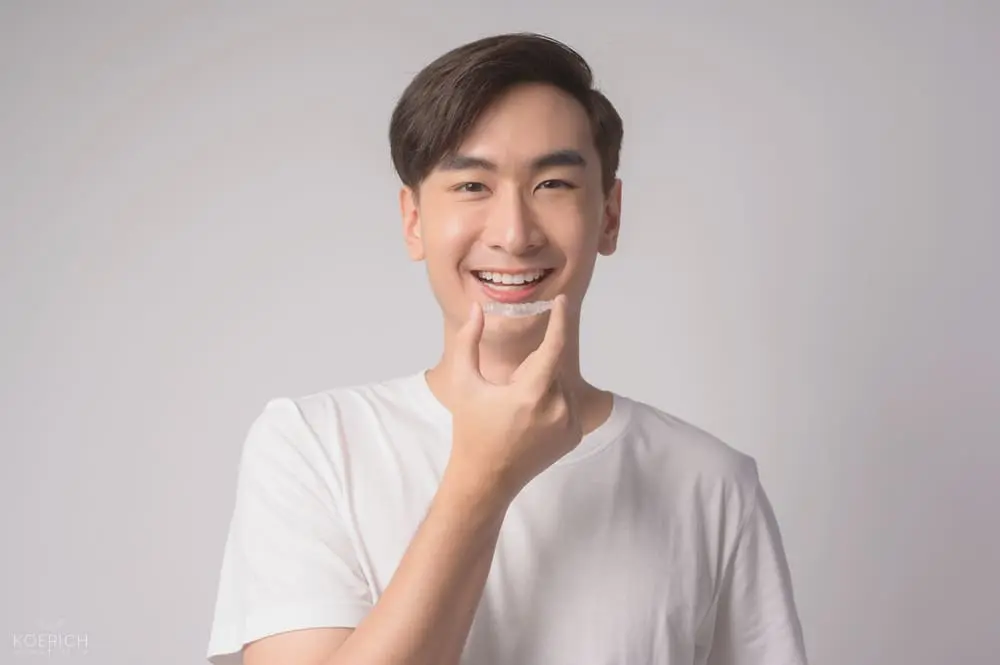 Smiling young man in a white t-shirt holds a clear aligner at Koerich Orthodontics in Charlotte, Indian Trail or Monroe, NC - How Long Does Invisalign Take in Charlotte, NC
